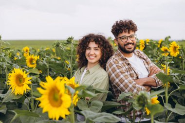 Two agronomists are posing with crossed arms in a sunflower field, showing their confidence and expertise in agriculture