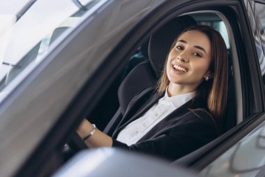 Happy saleswoman sitting inside a car holding the steering wheel and smiling, promoting car sales and customer satisfaction