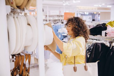 Customer selecting a stylish straw hat in a clothing store, enjoying the vibrant shopping experience for trendy summer accessories