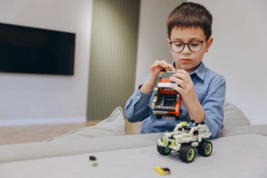 Young boy concentrating on assembling a toy car with colorful building blocks, developing fine motor skills and creativity in a comfortable home environment