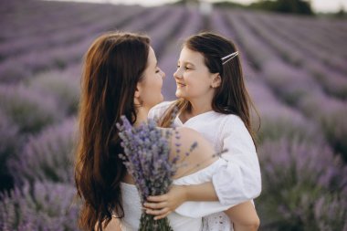 Mother and daughter smiling at each other while holding a vibrant lavender bouquet in a scenic lavender field, enjoying a joyful moment together