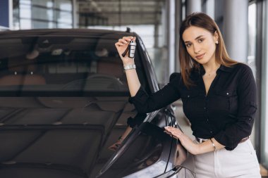 Saleswoman holding car keys while standing next to a new car in a dealership