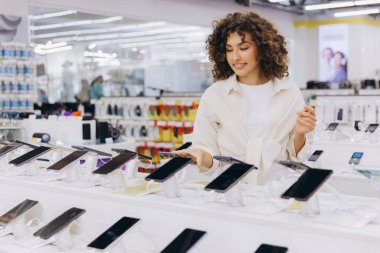 Customer comparing new smartphones in an electronics store, choosing the best mobile phone for her needs