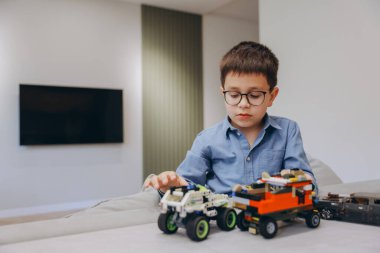 Smart little boy wearing glasses playing with building blocks toys on a table in the living room