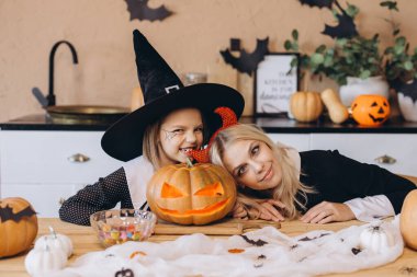 Mother and daughter smiling and having fun while preparing a carved pumpkin for Halloween party