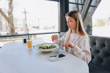 Young woman enjoying a fresh salad and orange juice in a bright restaurant, embracing a healthy lifestyle during her lunch break