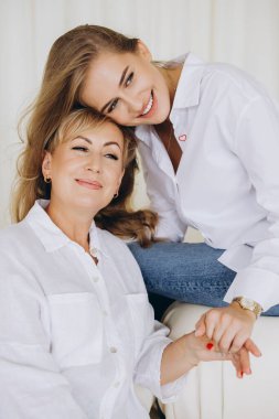 Happy daughter resting her head on her mother's shoulder, holding her hand and smiling, showing love, affection, and tenderness