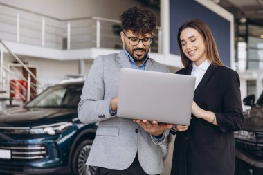 Salesman and customer collaborating over a laptop, discussing options while selecting a vehicle in a modern dealership showroom