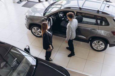 Salesperson demonstrating features of a new car to a customer inside a dealership, engaging in discussion about options and features