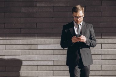 Businessman wearing suit and tie using smartphone in front of brick wall