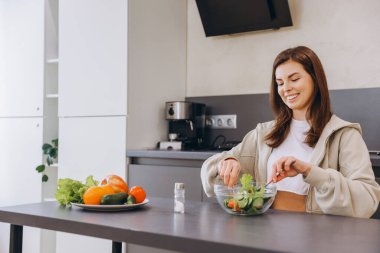 Smiling woman mixing fresh vegetables in a bowl, creating a vibrant salad in her modern kitchen, embracing a healthy lifestyle
