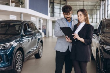 Salesman presenting a contract to businesswoman purchasing a new car at a dealership, highlighting a successful agreement in progress