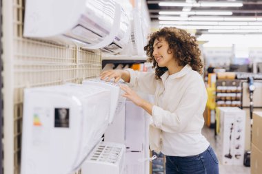 Customer comparing various air conditioner models while shopping in an electronics store, assessing features and making a purchase decision