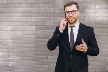 Confident businessman having a phone call and gesturing in front of a brick wall