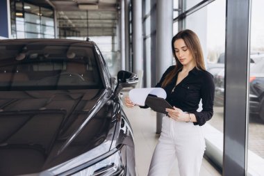 Saleswoman reading specifications of a new car in a dealership, holding documents and a folder