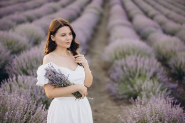 Young woman wearing a flowing white dress, holding a vibrant lavender bouquet while surrounded by a stunning lavender field in full bloom