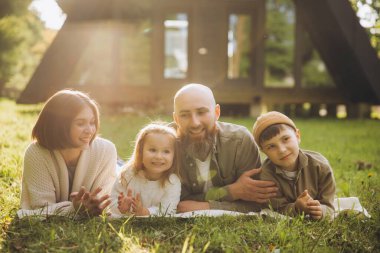 Family enjoying a relaxing weekend together, lying on the grass in front of their modern a frame cabin, embracing the joy of their time together