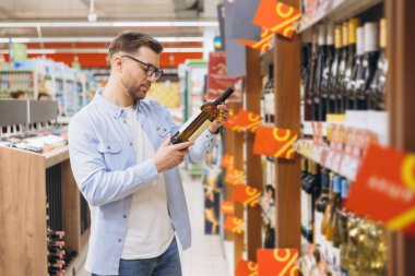 Customer checking wine bottle label during grocery shopping in supermarket alcohol section