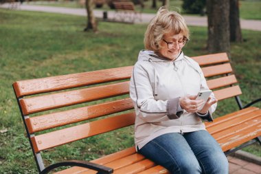 Happy elderly woman enjoying mobile technology outdoors, connecting with loved ones and staying active in her retirement