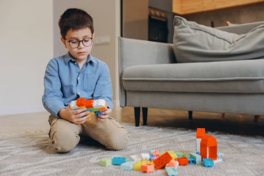 Child concentrating on building with colorful plastic blocks, developing fine motor skills and creativity in a comfortable home environment