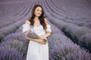 Fashion model wearing a flowing white dress, holding a vibrant lavender bouquet while posing gracefully in a blooming lavender field