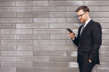 Businessman wearing suit and tie using mobile phone standing next to a modern brick wall