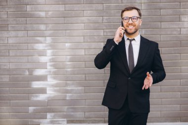 Smiling businessman having a phone call while standing against a brick wall