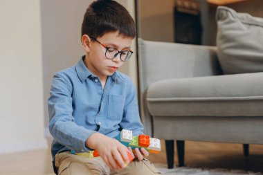 Smart boy concentrating on building something with colorful plastic bricks, sitting on the floor in the living room