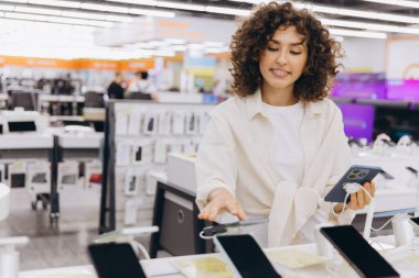 Customer comparing new smartphones in an electronics store, choosing the best mobile phone for her needs