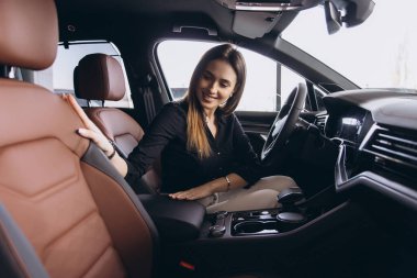 Young woman choosing new automobile at car dealership, touching leather seat and checking interior