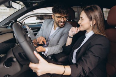 Salesman showing car features on a tablet to a businesswoman in a car dealership