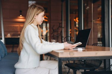 Freelancer working remotely in a modern cafe, using a laptop and smartphone while enjoying a cozy atmosphere and urban views