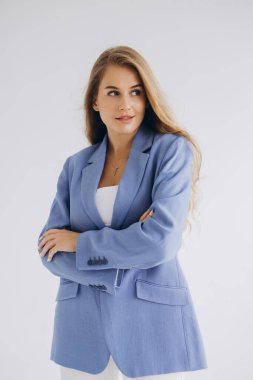 Confident young businesswoman crossing her arms and wearing a blue jacket and white shirt, looking away on a white background