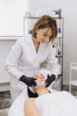 Professional beautician applying a rejuvenating facial cleansing mask to a client in a serene beauty salon, enhancing skin health and relaxation