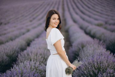 Young woman wearing a flowing white dress, holding a vibrant lavender bouquet while surrounded by a breathtaking lavender field