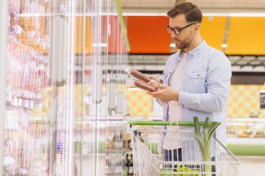 Man selecting salami package from refrigerated section in grocery store