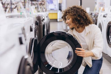 Customer examining washing machine drum in electronics store, making purchasing decision for home appliance