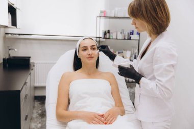 Beautician wearing black gloves applying cream on a woman's face during a beauty treatment in a professional beauty salon
