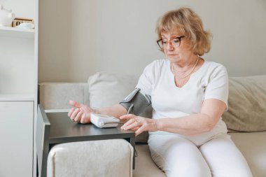 Elderly woman taking care of her health, measuring blood pressure at home using a digital blood pressure monitor