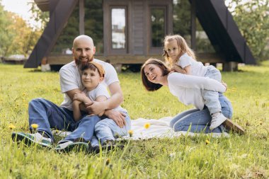 Smiling parents and children having fun on a blanket in their backyard, enjoying quality time together near their cozy home
