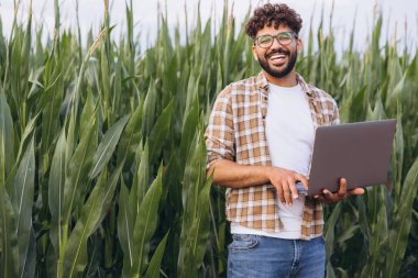 Smiling agronomist working with a laptop in a vibrant corn field, utilizing technology to enhance agricultural practices and productivity