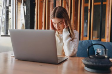 Freelancer suffering from headache while working remotely on laptop in cafe, massaging temples and closing eyes from pain