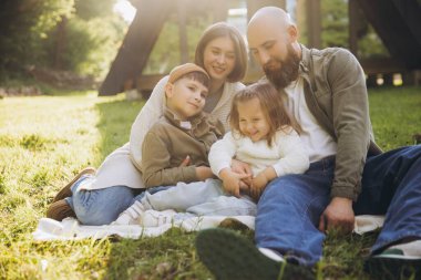 Smiling family gathered on a blanket in the park, enjoying a sunny autumn day filled with laughter, love, and playful moments together