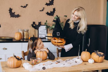 Mother and daughter joyfully decorating their home for Halloween, carving pumpkins and sharing fun moments together in the kitchen