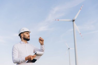 Engineer with a clipboard is inspecting wind turbines in a field, contributing to sustainable energy production