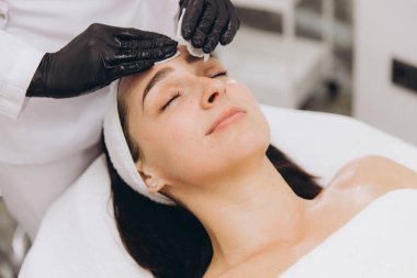 Beautician gently applying cream to a relaxed woman's face, showcasing skincare treatment in a professional salon environment