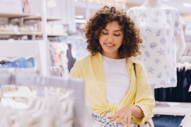 Smiling curly haired woman shopping for clothes in a fashion store, enjoying her retail therapy