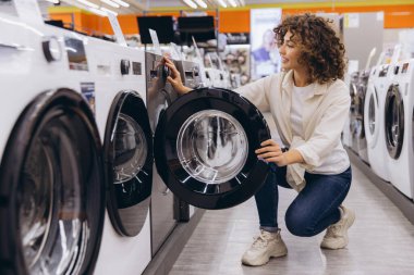 Customer browsing and selecting a modern washing machine in an electronics store, surrounded by various options and appealing displays