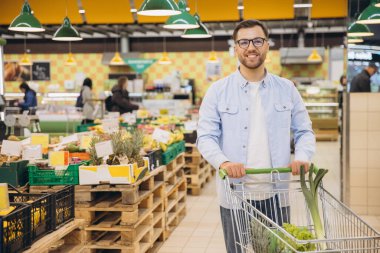 Customer choosing fresh vegetables inside supermarket with shopping cart