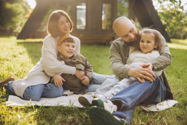 Smiling parents embracing their children while sitting on a cozy blanket in the backyard of a modern home, enjoying quality family time